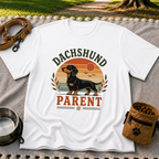 White T-shirt mockup featuring dachshund portrait in a striped sunset badge with Dachshund Parent lettering.