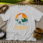 Sport Grey T-shirt mockup featuring Bigfoot and a dog walking through pine trees beneath an orange sunset.