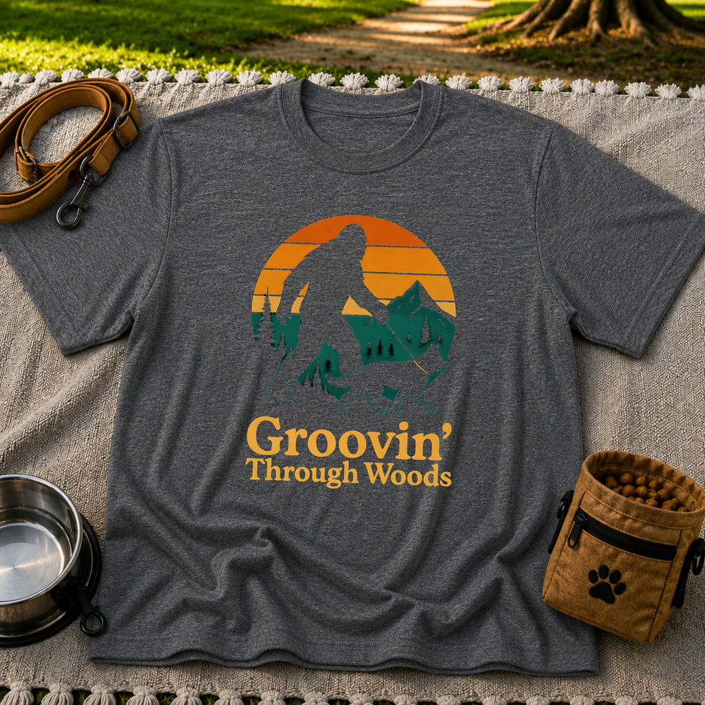 Dark Heather Grey T-shirt mockup featuring Bigfoot and a dog walking through pine trees beneath an orange sunset.