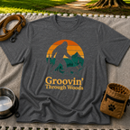 Dark Heather Grey T-shirt mockup featuring Bigfoot and a dog walking through pine trees beneath an orange sunset.
