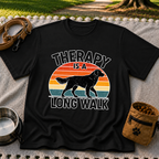 Black T-shirt mockup featuring dog silhouette walking across a striped sunset beneath Therapy Is a Long Walk.