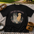 Black T-shirt mockup featuring golden-coated dog beside floral cowboy boots and flowers beneath Stay Wild Sweet Soul.