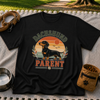 Black T-shirt mockup featuring dachshund portrait in a striped sunset badge with Dachshund Parent lettering.