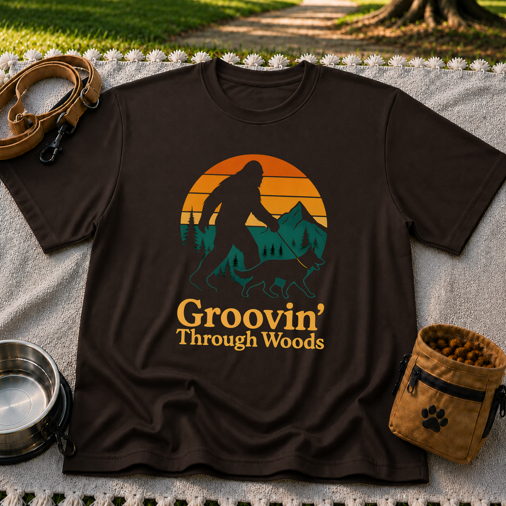Dark Chocolate T-shirt mockup featuring Bigfoot and a dog walking through pine trees beneath an orange sunset.