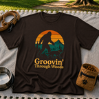 Dark Chocolate T-shirt mockup featuring Bigfoot and a dog walking through pine trees beneath an orange sunset.