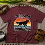 Maroon T-shirt mockup featuring dog silhouette walking across a striped sunset beneath Therapy Is a Long Walk.