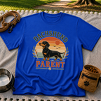 Royal T-shirt mockup featuring dachshund portrait in a striped sunset badge with Dachshund Parent lettering.