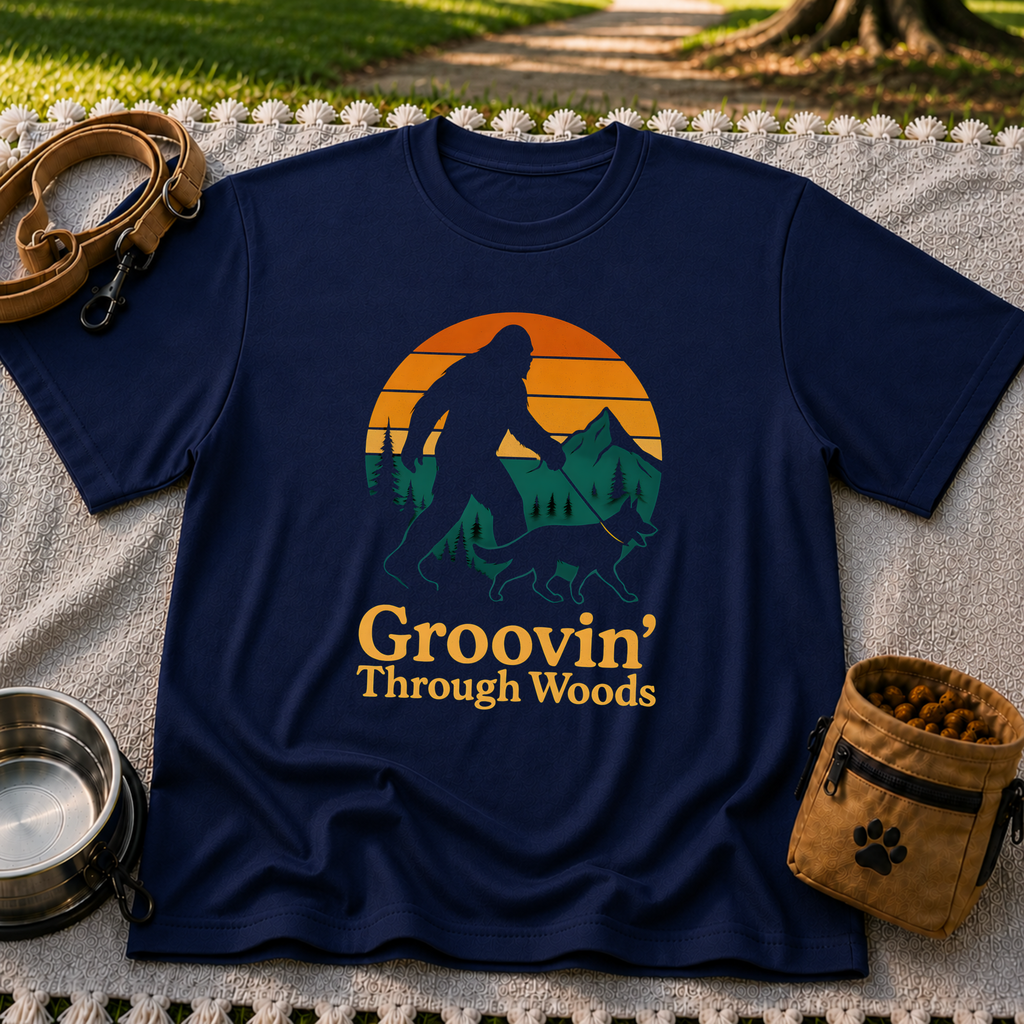 Navy T-shirt mockup featuring Bigfoot and a dog walking through pine trees beneath an orange sunset.